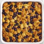 Baked blueberry bread pudding in a white dish with golden bread cubes.
