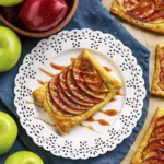 Caramel apple tart with puff pastry and sliced apples on a white plate.