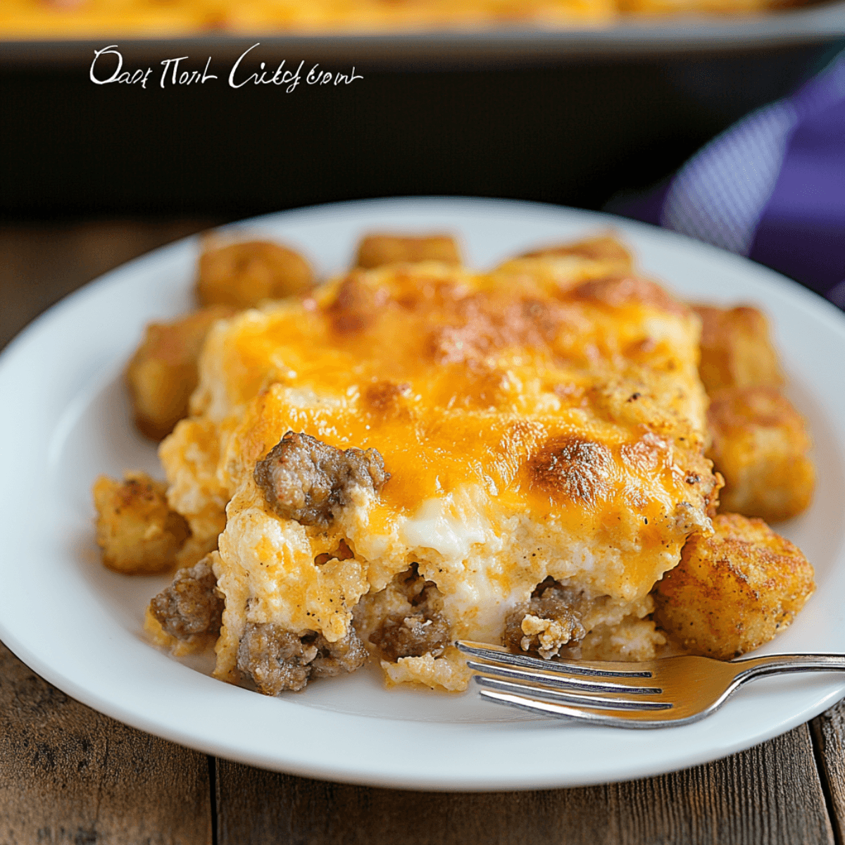 Close-up of cheesy sausage tater tot breakfast casserole served on a white plate with fork on rustic table.