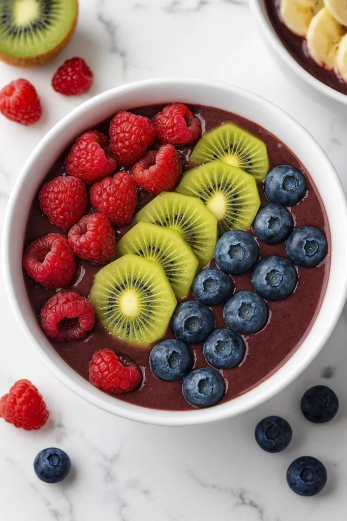 Top-down view of a vibrant acai bowl with raspberries, kiwi slices, and blueberries on marble