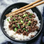 Korean-style ground beef with white rice topped with sesame seeds and green onions in a black bowl with chopsticks