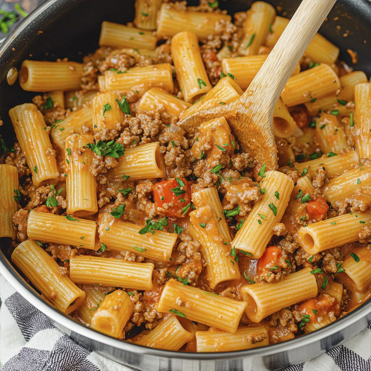 Creamy rigatoni pasta with ground beef and tomatoes in a white bowl with parsley garnish
