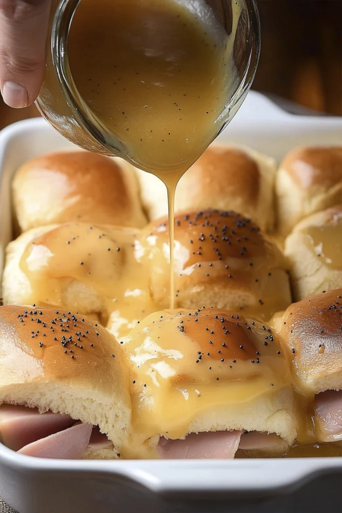 Freshly baked ham and cheese slider with melted cheese and poppy seeds being lifted from a casserole dish.