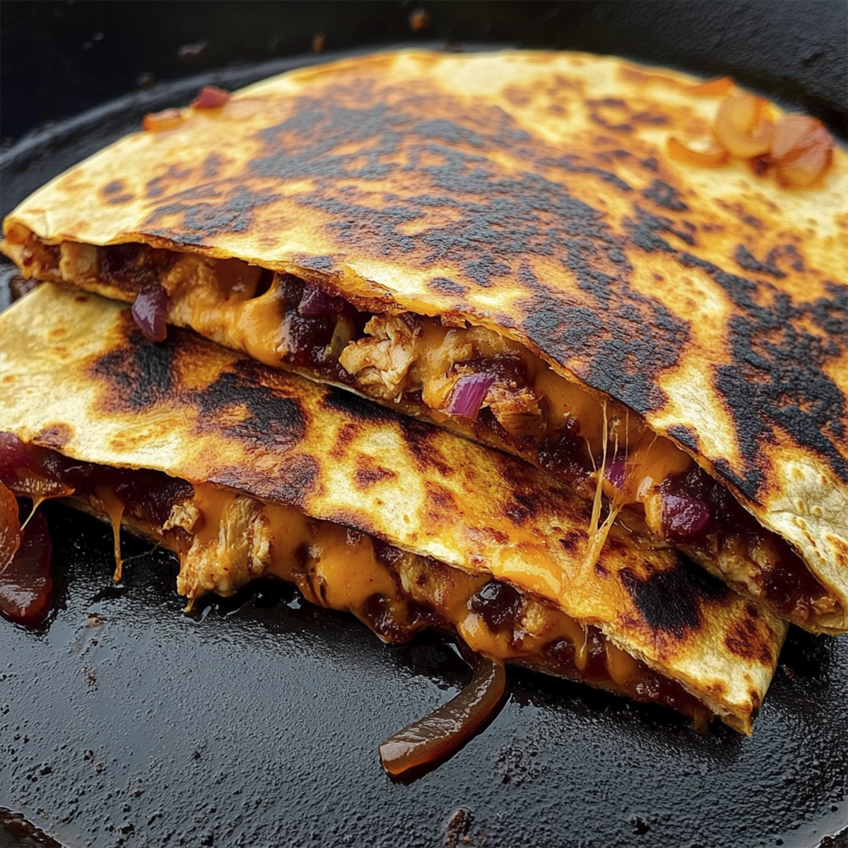 Close-up of a crispy BBQ chicken quesadilla with melted cheddar cheese and caramelized onions cooked in a cast iron skillet.