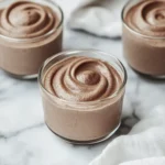 Creamy chocolate mousse swirled in clear glass cups on a marble background.