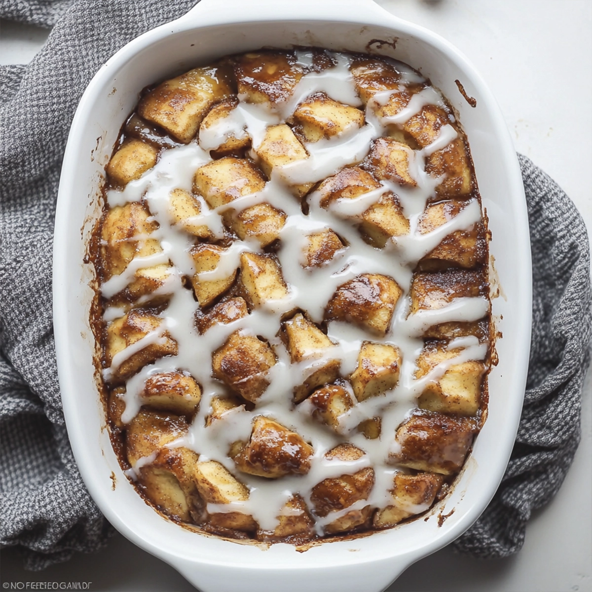 Top-down view of cinnamon apple bake with cream cheese glaze in a white casserole dish.