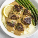 Seared steak medallions topped with creamy garlic pepper sauce served with mashed potatoes and asparagus.