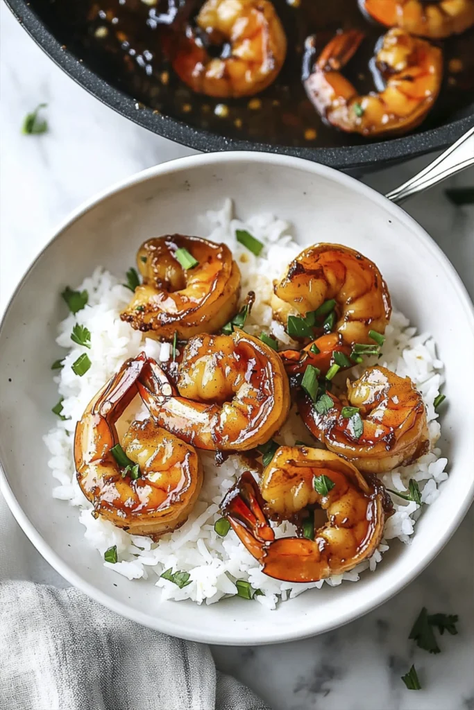 Overhead view of honey garlic shrimp served over fluffy white rice with green onion garnish on a marble surface.