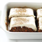 Carrot cake bars with thick cream cheese frosting and cinnamon dusting in a white baking dish.