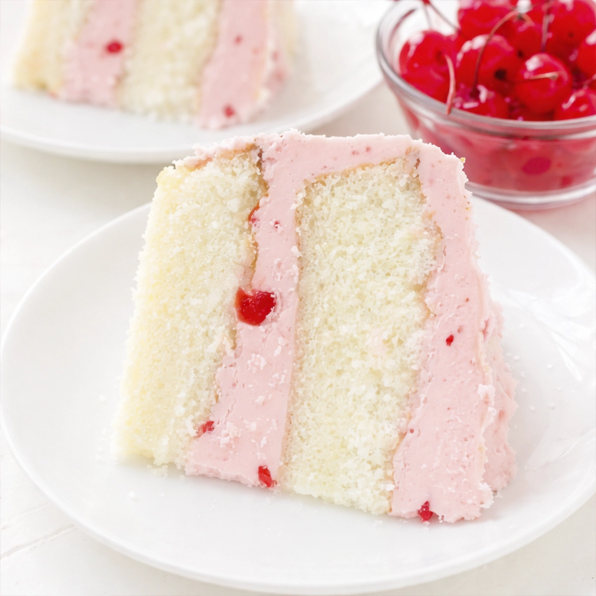 Slice of cherry layer cake with pink frosting and maraschino cherry filling on a white plate