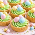 Mini Easter tart desserts with green buttercream frosting and pastel chocolate candy eggs on top.