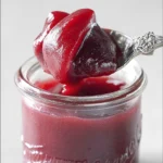 Close-up of a spoon scooping thick homemade rhubarb sauce from a glass jar.