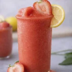 Frozen strawberry lemonade slush in a tall glass topped with a fresh strawberry slice and lemon wheel garnish.