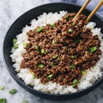 Korean ground beef rice bowl topped with sesame seeds and green onions in a black bowl with chopsticks
