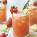 Tropical strawberry pineapple mocktail in a clear glass with lime wedge, fresh strawberry, and pineapple leaf garnish on a white marble surface.