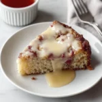 Slice of homemade strawberry coffee cake with vanilla glaze on a white plate beside a cup of tea.