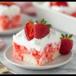 Strawberry poke cake slice with whipped cream frosting and fresh strawberry topping on a white plate.