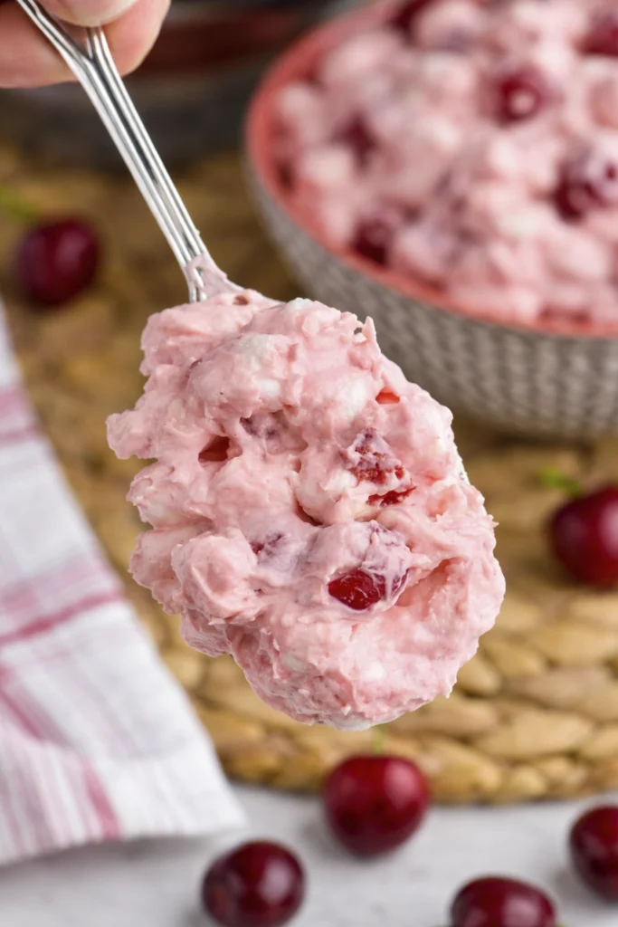 Square slice of cherry cheesecake with graham cracker crust and glossy cherry topping lifted on a cake server above the remaining cheesecake.