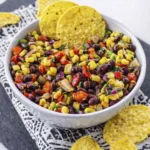 Corn and black bean salad with diced vegetables served in a white bowl with tortilla chips