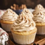 Vanilla cupcakes topped with cinnamon buttercream frosting on a rustic wooden table