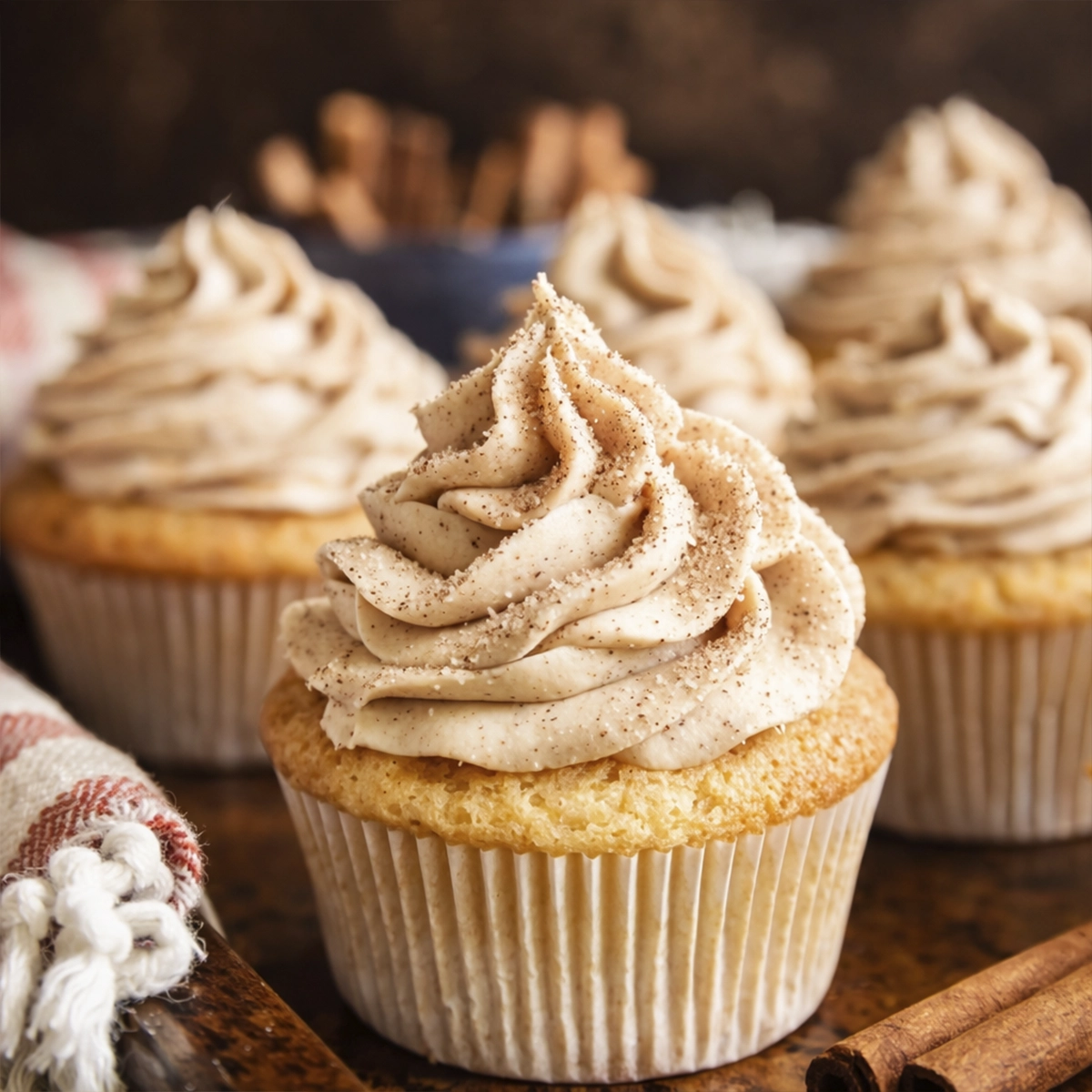 Vanilla cupcakes topped with cinnamon buttercream frosting on a rustic wooden table