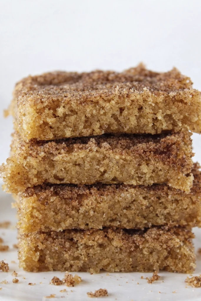 Stack of homemade cinnamon sugar blondie bars with soft crumb and cinnamon topping on a white background