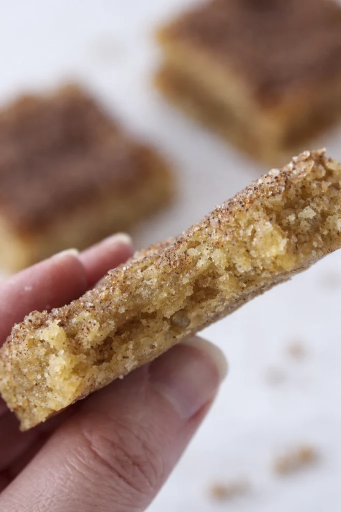 Hand holding a chewy cinnamon sugar blondie bar showing soft crumb and cinnamon topping