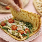 Hand folding a golden crepe filled with grilled chicken, arugula, cherry tomatoes, and pesto sauce