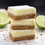 Stacked lime dessert bars with creamy filling and crumb crust topped with powdered sugar and fresh lime slices