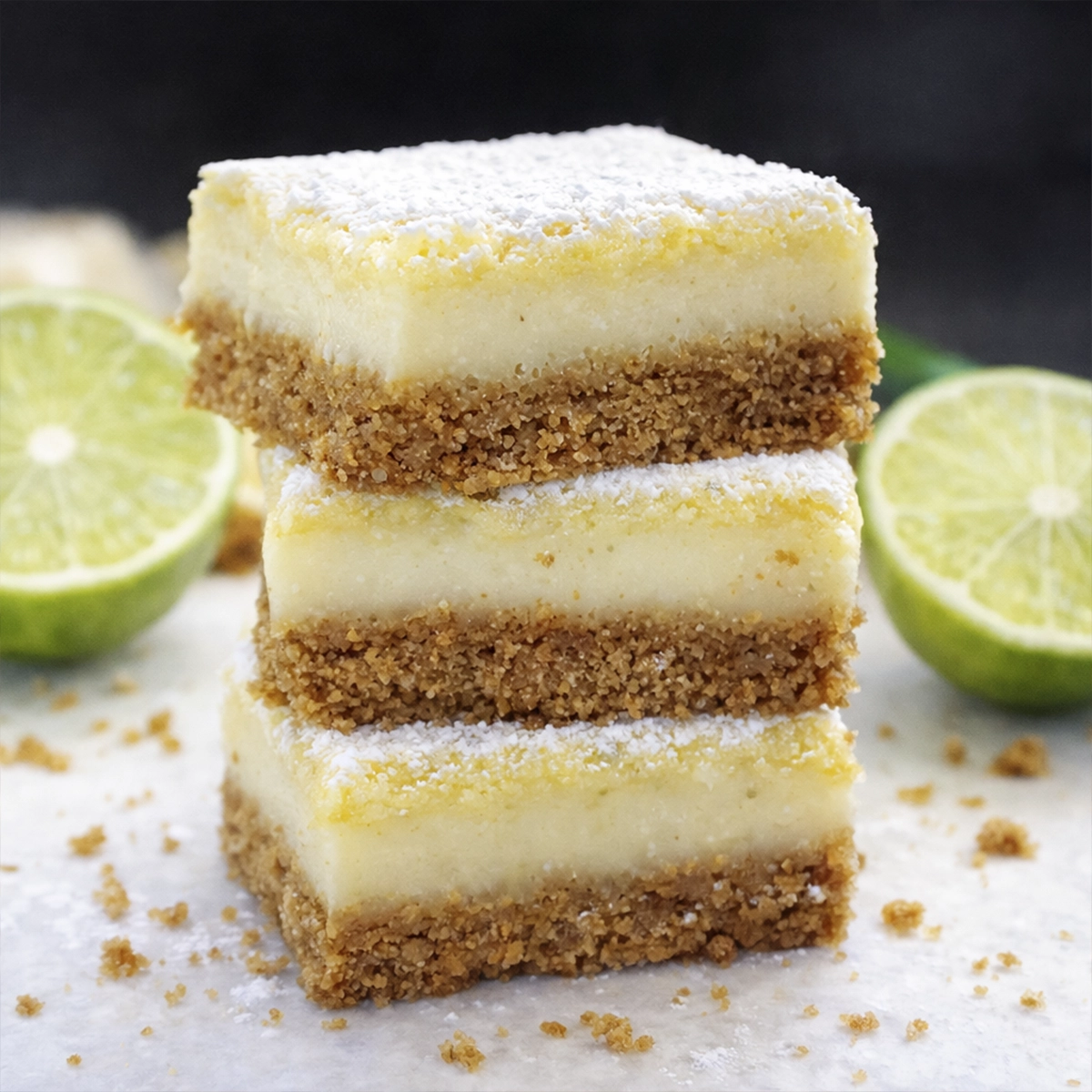 Stacked lime dessert bars with creamy filling and crumb crust topped with powdered sugar and fresh lime slices