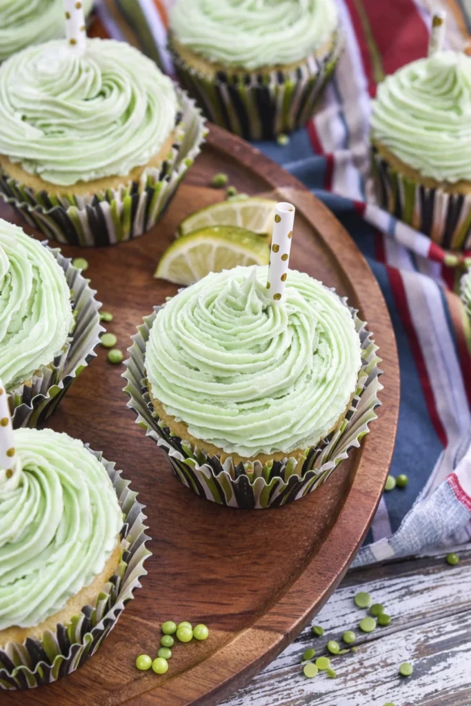 Pastel green frosted lime cupcakes on a wooden tray with lime wedges and festive party decor.