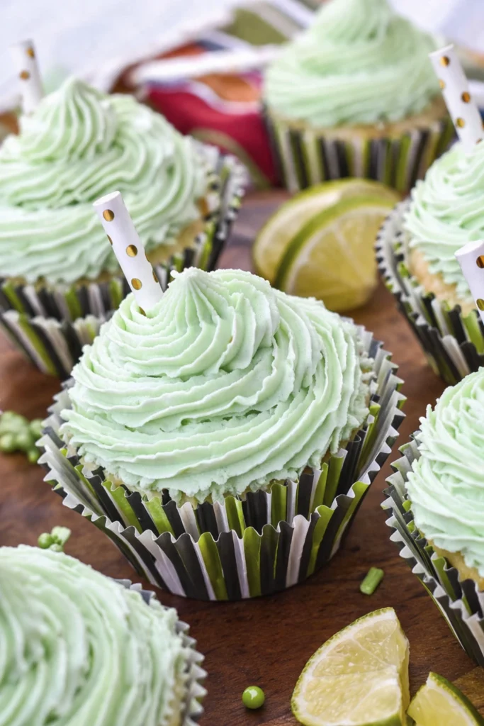 Mint green frosted cupcakes with swirled buttercream on a wooden board with lemon slices and decorative sprinkles.