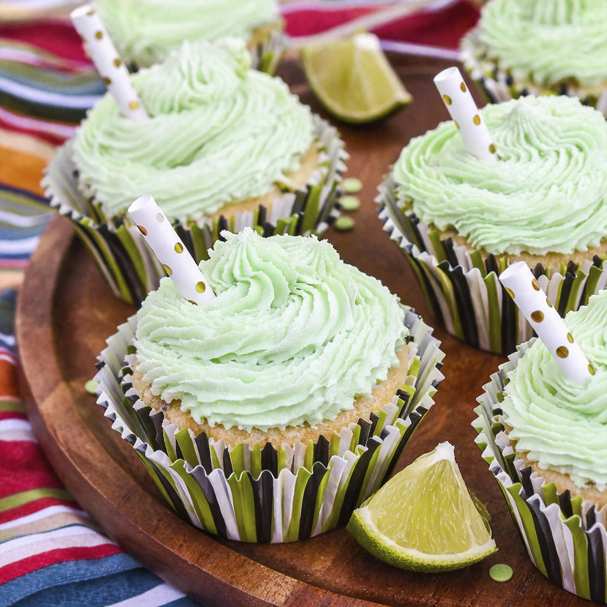 Mint green frosted cupcakes with swirled buttercream frosting, striped liners, and lemon lime slices on a wooden table.