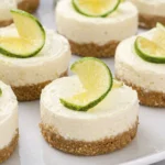 Mini lime cheesecakes with graham cracker crust topped with fresh lime slices on a white plate.
