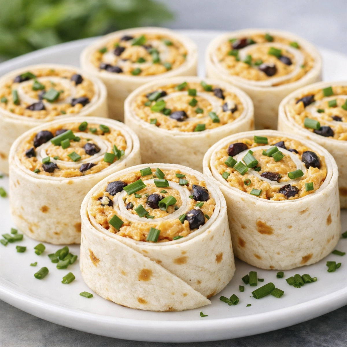 Creamy tortilla pinwheel wraps filled with cheese spread and herbs, sliced into bite-sized appetizers and arranged on a white plate.
