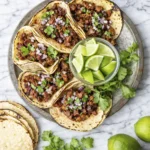 Authentic Mexican street tacos with grilled tortillas, carne asada, diced onions, cilantro, and fresh lime wedges on a marble background