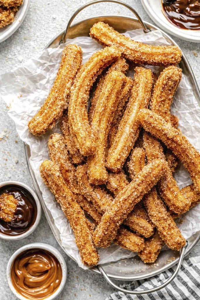 Close-up of crispy cinnamon sugar churros with caramel dipping sauce and sugar coating in a tray