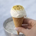 Hand holding a vanilla ice cream cone topped with crushed pistachios against a soft background