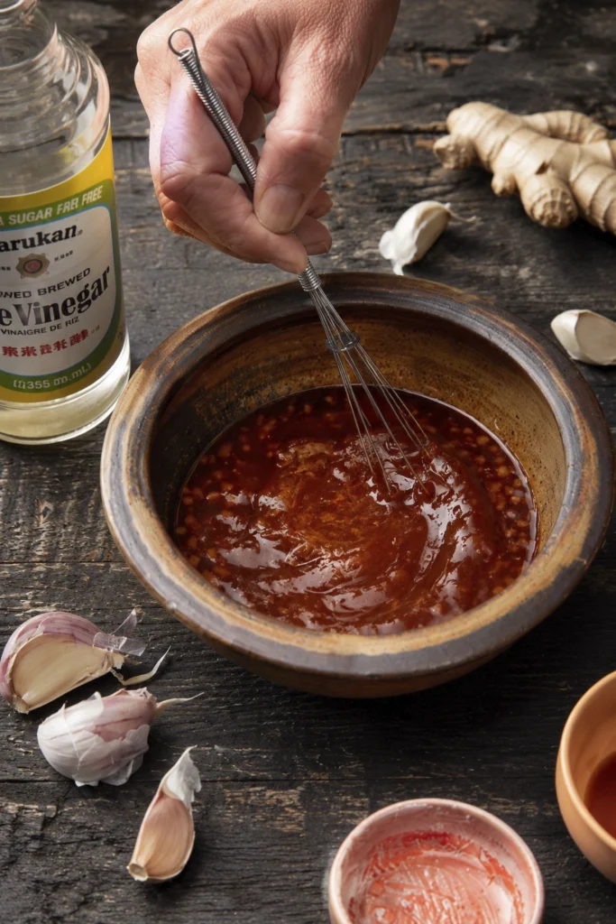 Whisking homemade savory sauce with garlic ginger and rice vinegar in a rustic bowl