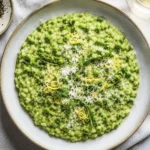 Overhead view of a creamy rice and pea dish topped with Parmesan cheese, lemon zest, and fresh pea shoots