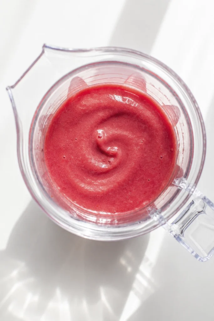 Homemade fruit sauce in a glass jar with fresh rhubarb pieces on a marble surface