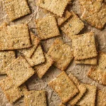 Hand scoring seasoned cracker dough into squares on a parchment lined baking sheet before baking