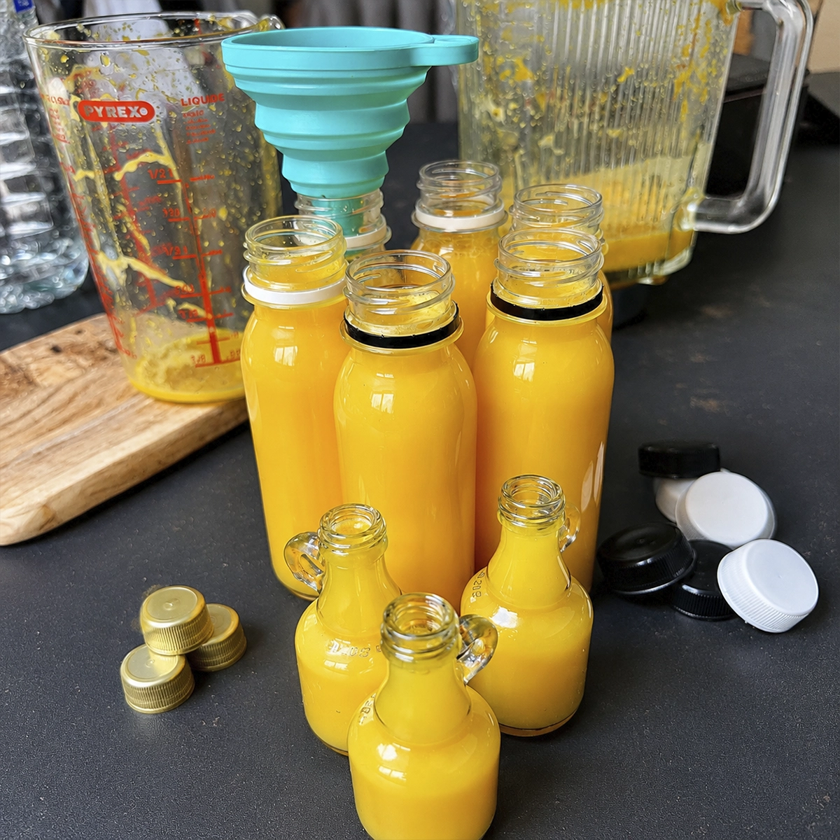 Fresh turmeric and citrus juice being strained through a fine mesh sieve into a measuring cup on a kitchen counter