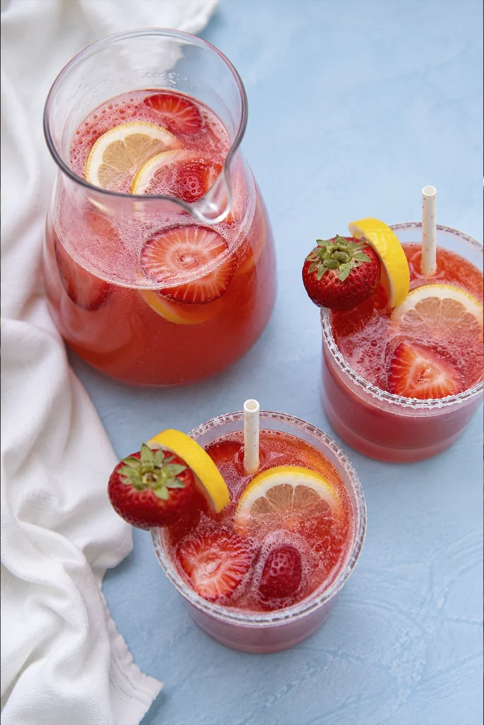 Refreshing homemade berry and lemon drink served with fresh fruit in glasses beside a glass pitcher.