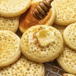 Hand holding a stack of Moroccan baghrir pancakes topped with melting butter and honey, highlighting the signature honeycomb texture.