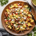 Overhead view of authentic Mexican chilaquiles with scrambled eggs, queso fresco, tomatoes, onions, and cilantro on a rustic ceramic plate.