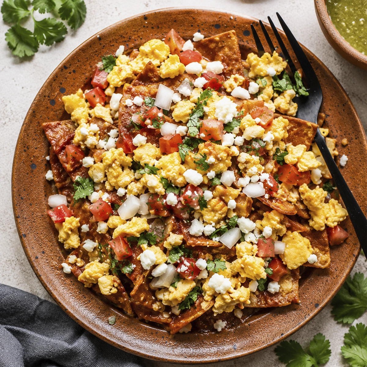 Overhead view of authentic Mexican chilaquiles with scrambled eggs, queso fresco, tomatoes, onions, and cilantro on a rustic ceramic plate.