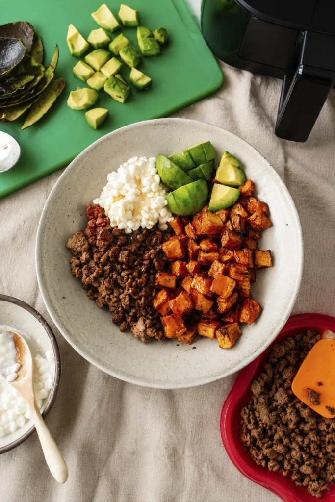 Homemade beef bowl prepared with roasted sweet potatoes, avocado, and cottage cheese on a kitchen table