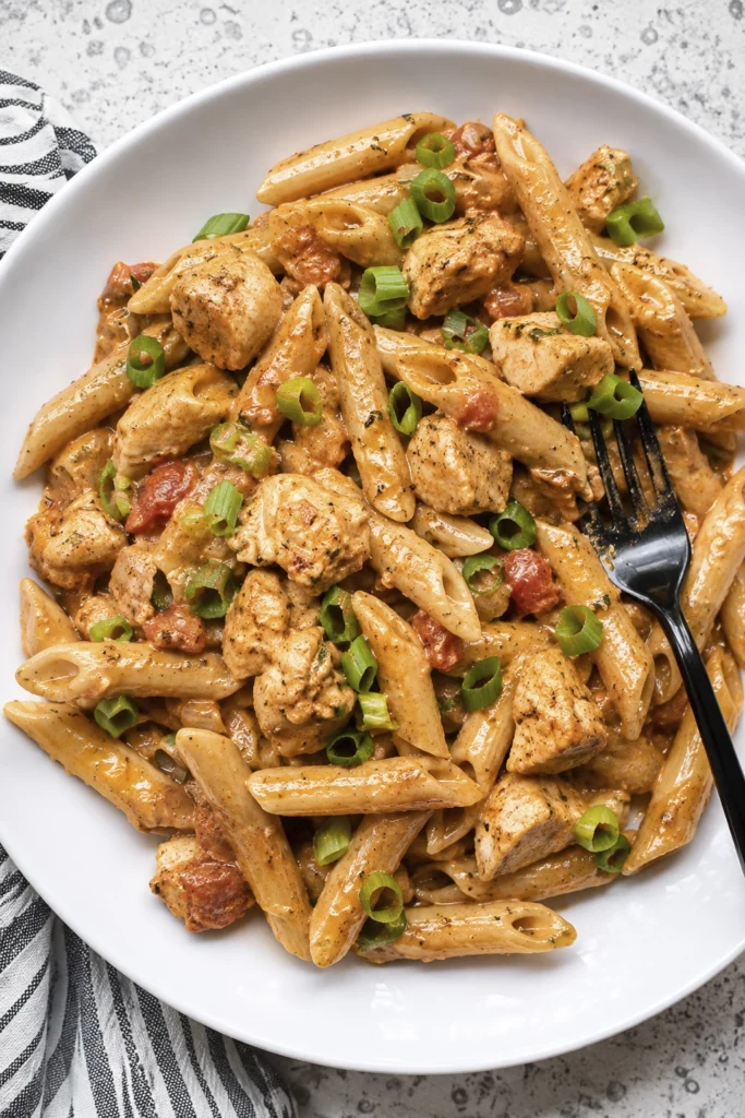 Creamy Cajun chicken penne pasta with tomatoes and green onions served on a white plate.