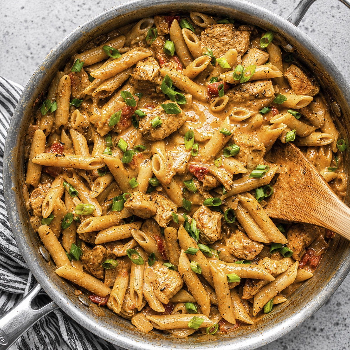 Creamy Cajun chicken penne pasta with green onions in a skillet.